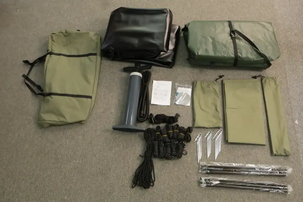 Outdoor camping gear including bags, a flashlight, and stakes on a gray surface.
