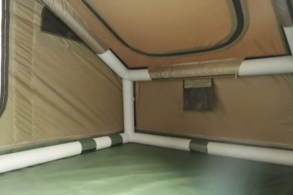 Innenansicht eines Campingzelts mit beigefarbenem Stoff und weißen Stangen.