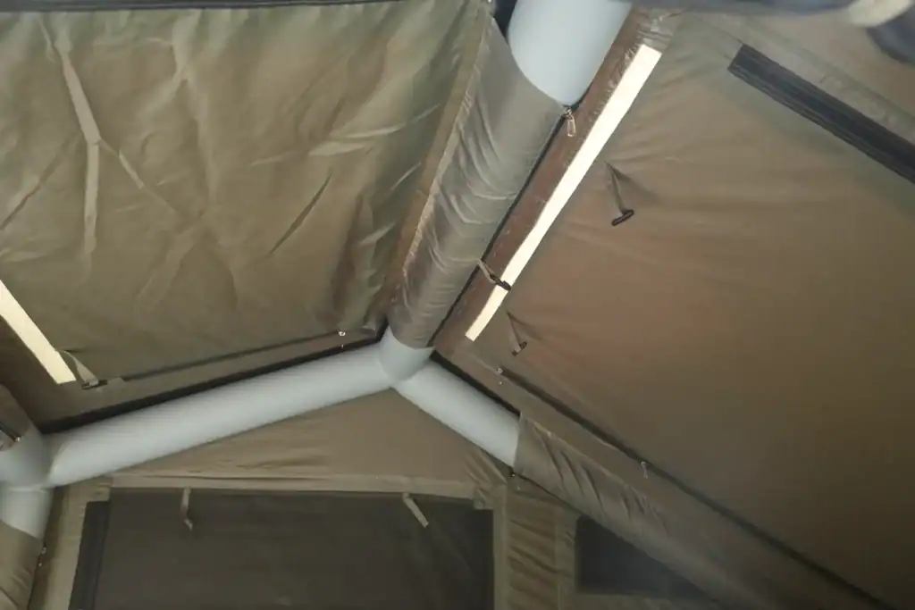 Industrial tent ceiling with pipes and lighting fixtures.